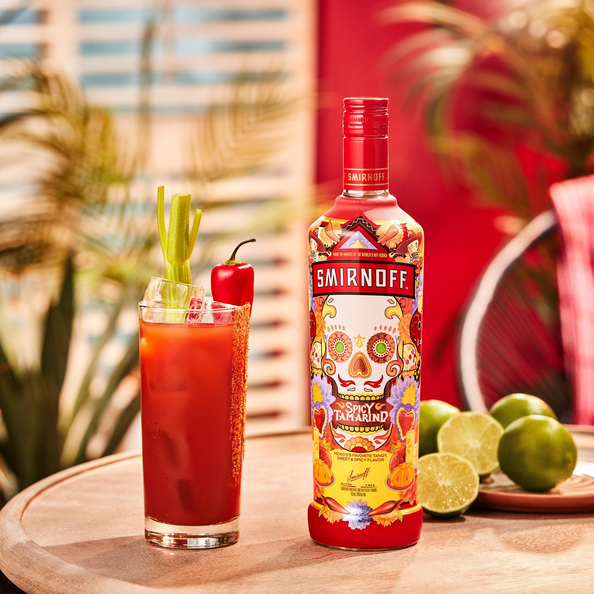 Smirnoff Spicy Tamarind vodka bottle alongside a red colored Spicy Bloody cocktail with spicy seasoning and celery garnish. 
