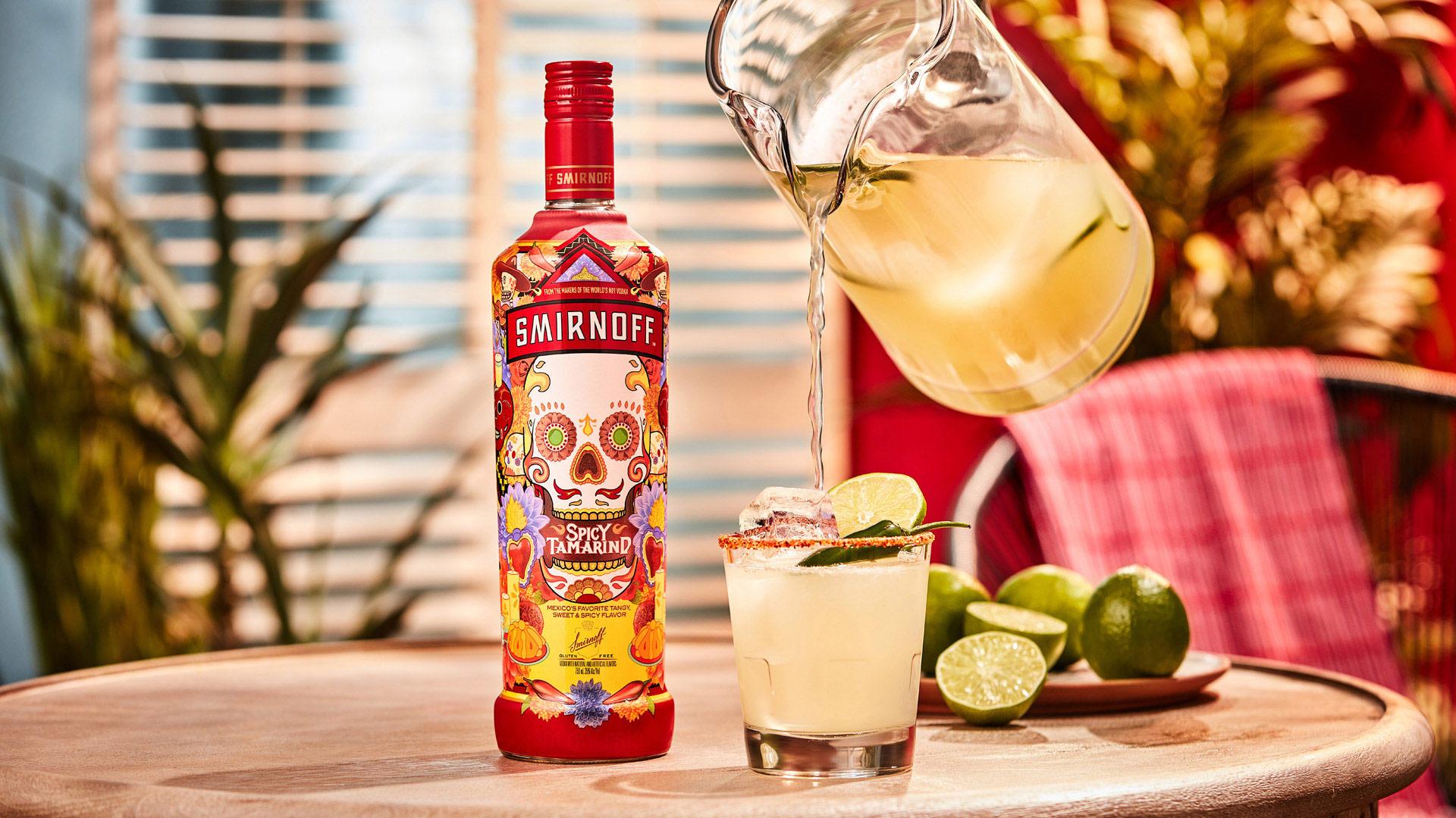 Smirnoff Spicy Tamarind vodka bottle alongside a pitcher pouring a Spicy Tama-rita cocktail with a spicy seasoning rim,  lime wheel and jalepeno for garnish. 