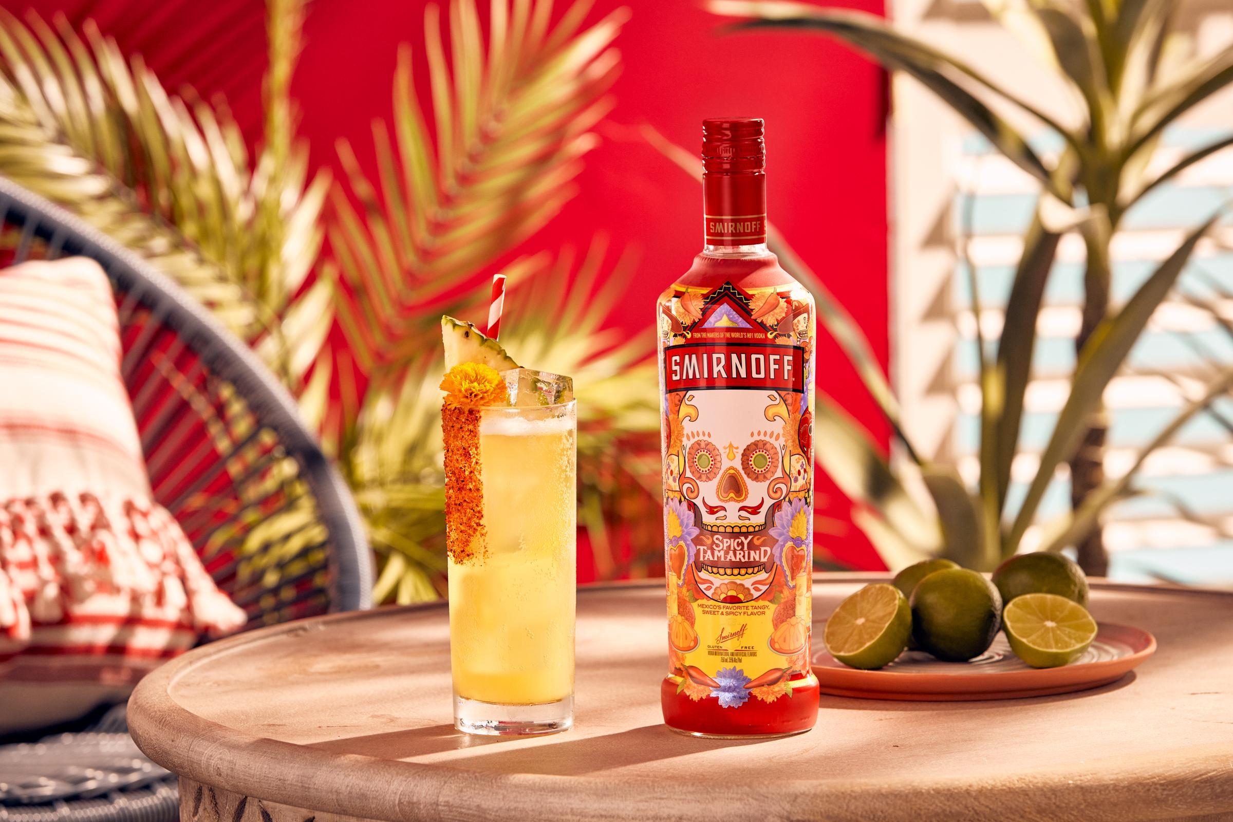Smirnoff Spicy Tamarind vodka bottle alongside a yellow colored Pina Picante cocktail with a spicy rim, pineapple wedge and flower for garnish.