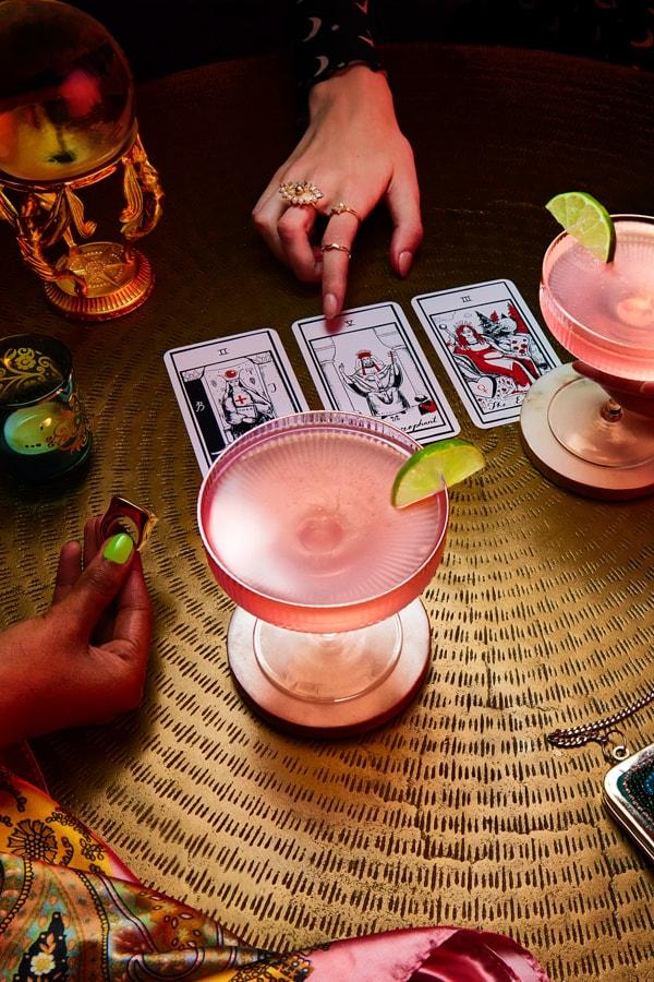 Two people reading tarot cards drinking Pink Cosmo
