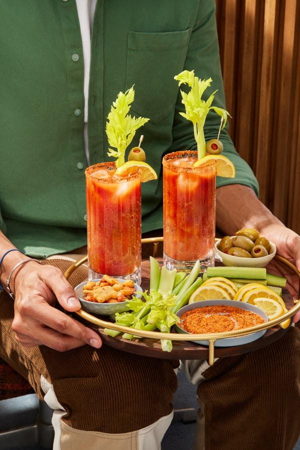 Two Bloody Mary’s on a tray accompanied by the ingredient