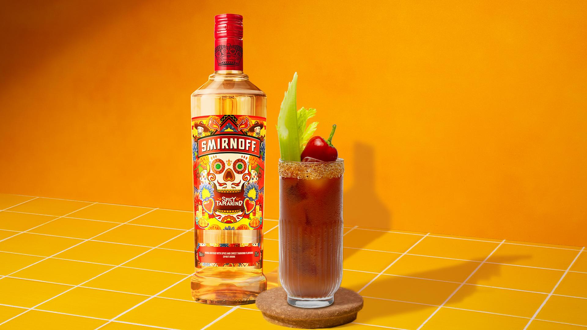 Smirnoff Spicy Tamarind vodka bottle beside a Bloody Mary cocktail with a chili powder rim, garnished with a celery stalk and a red chili pepper, set against a vibrant yellow background with white grid lines.