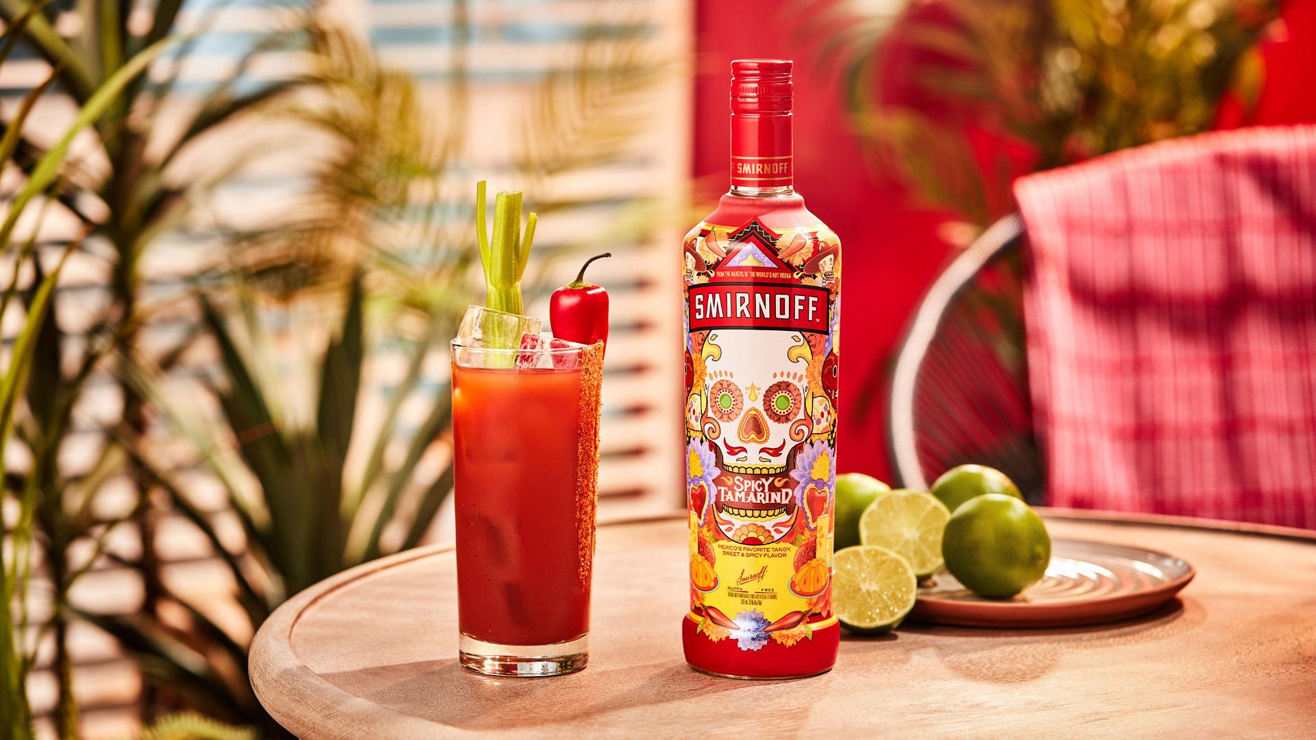 Smirnoff Spicy Tamarind vodka bottle alongside a red colored Spicy Bloody cocktail with spicy seasoning and celery garnish. 